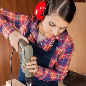 Person using a power drill with safety goggles and ear protection indoors. 